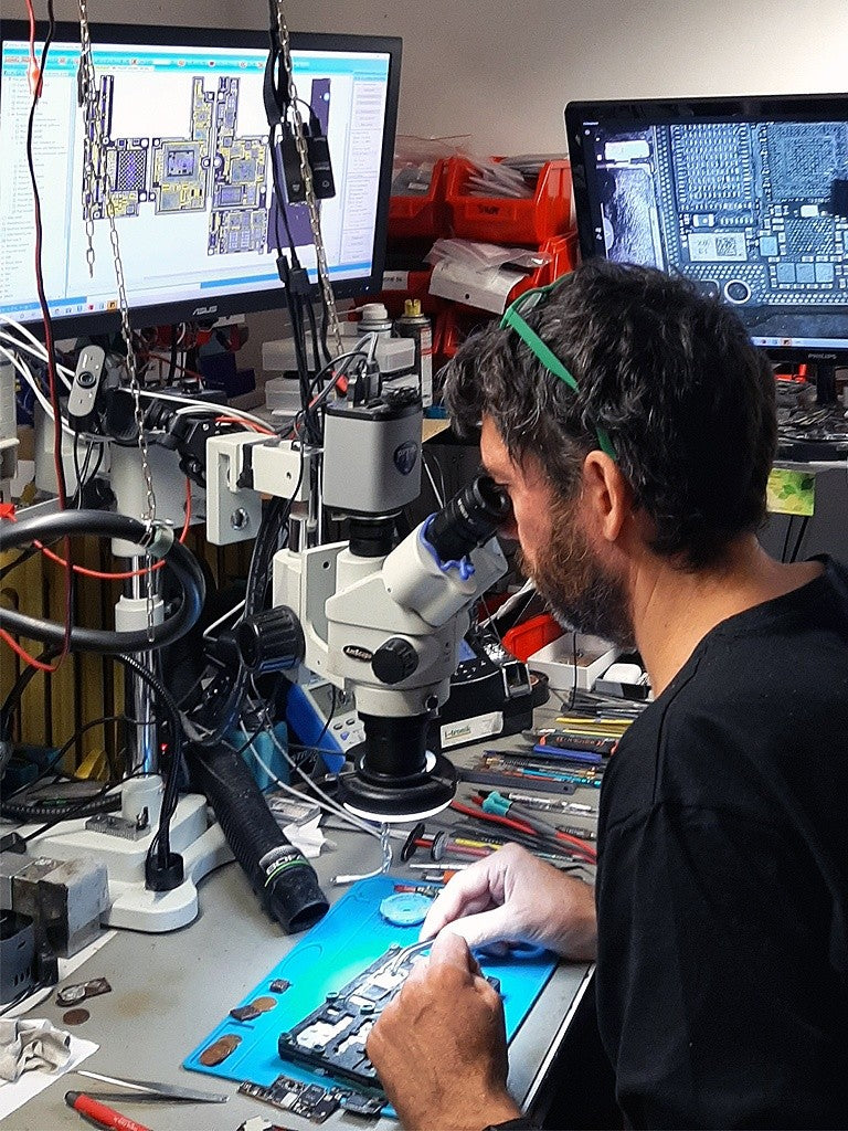 A Nous Globals technician repairing a motherboard under a microscope
